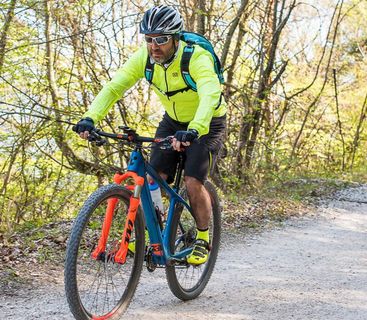 Aktiver Radsportler genießt eine sonnige Tour durch den Wald. Ein Mountainbiker in neongelber Jacke und Helm fährt auf einem Waldweg.