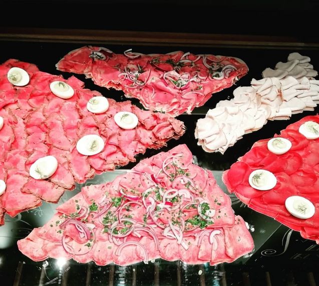 Verschiedene Scheiben von aufgeschnittenem Aufschnitt mit Zwiebeln, Eiern und Kräutern garniert.