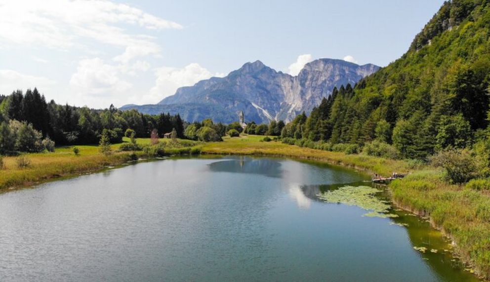 Friedliche Alpenidylle am smaragdgrünen See inmitten majestätischer Gipfel. Ein idyllischer Bergsee in den Alpen, umgeben von grünen Wiesen, dichten Wäldern und einer kleinen Kirche in der Ferne vor einer imposanten Bergkulisse.