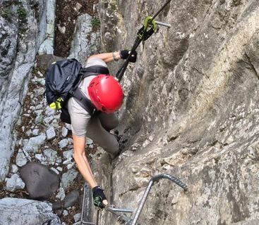 Abenteuer am Fels: Ein spannender Aufstieg durch eine enge Schlucht. Eine Person beim Klettern an einer steilen Felswand in einem Klettersteig mit rotem Helm und Rucksack.