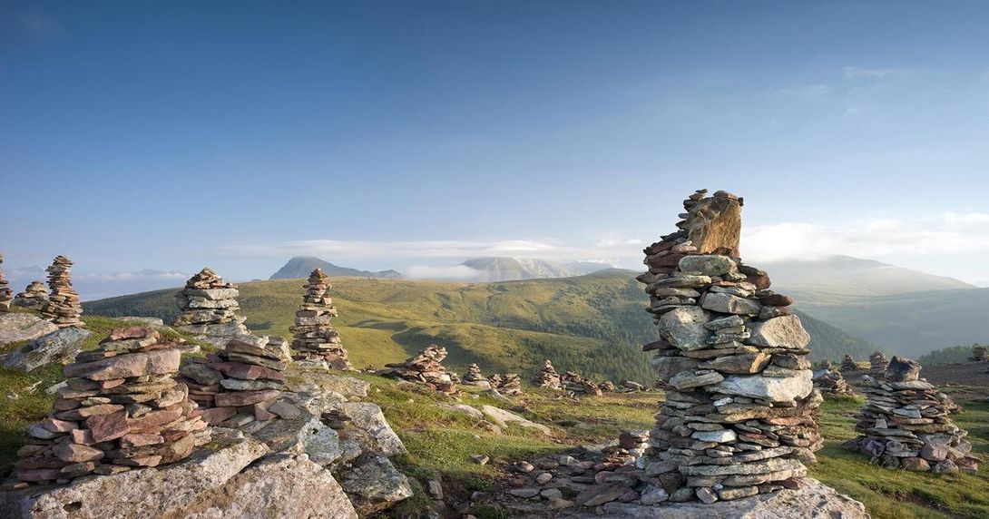 Stille Wächter aus Stein in den weiten Höhen der Alpen Eine weitläufige Bergwiese mit vielen aufgeschichteten Steinmännchen vor einer Bergkette bei klarem Himmel.