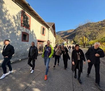 Eine Gruppe von Menschen, die auf einer Straße neben einem alten Gebäude und Bergen im Hintergrund spazieren.